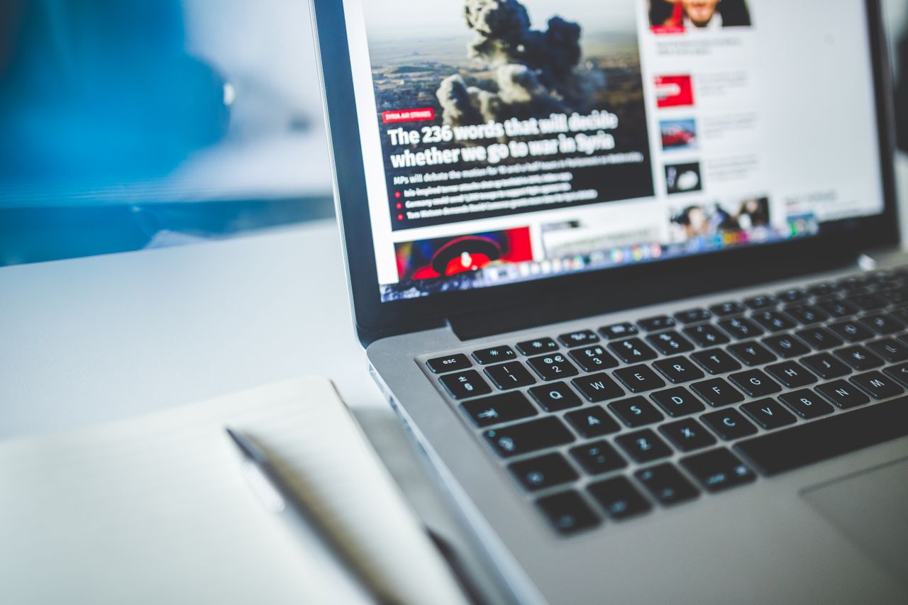 Services Open laptop displaying an online news article on a desk with a notebook nearby.