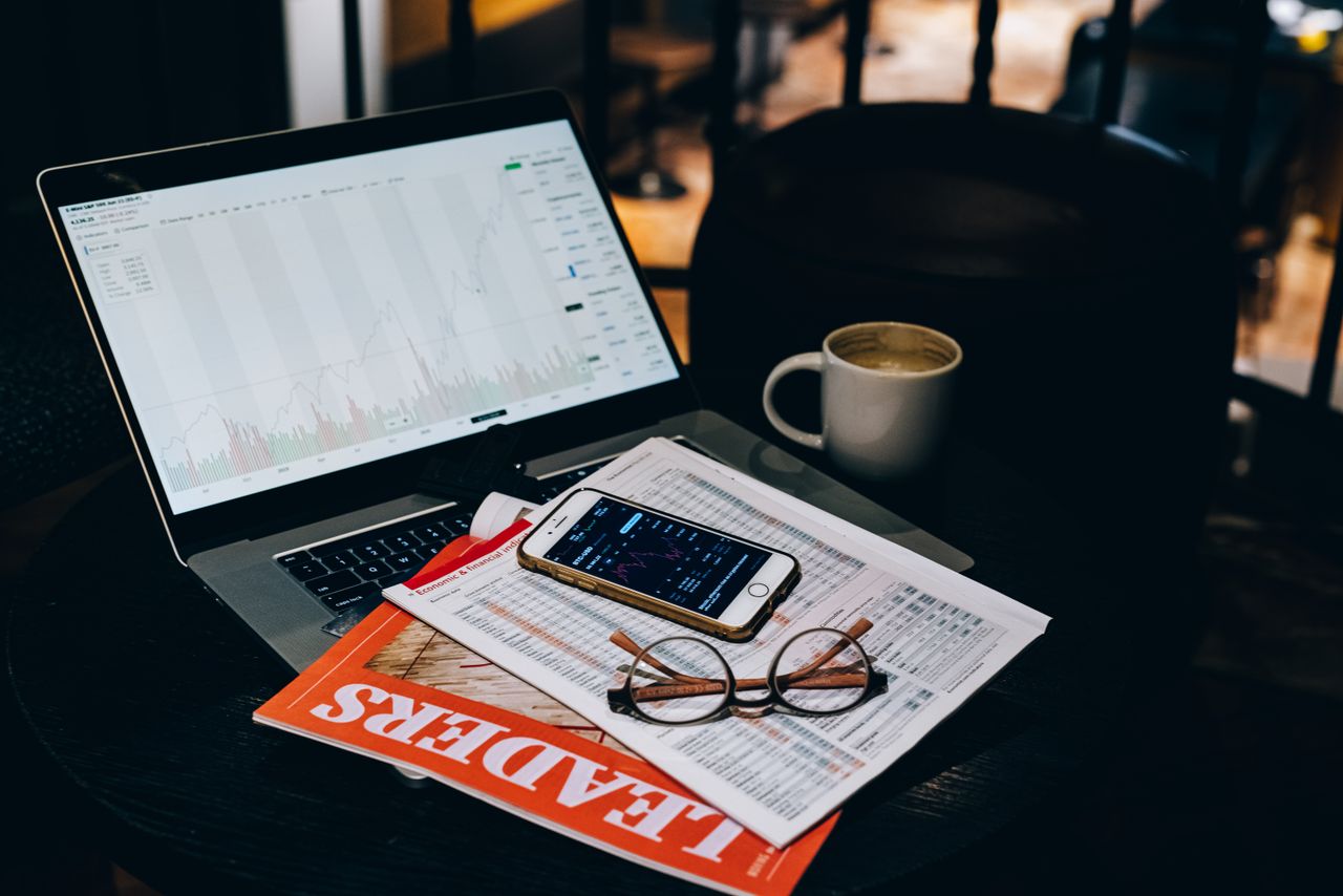 About A cozy office desk setup with a laptop displaying stock charts, coffee, and documents.